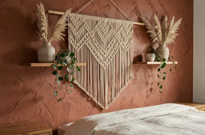 Mur décoratif en macramé naturel avec étagères en bois et plantes séchées dans une chambre au style bohème terracotta